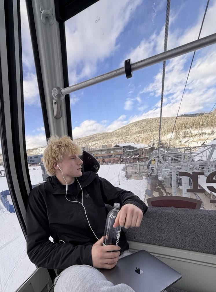 Riding a ski gondola with a laptop, snowy resort below