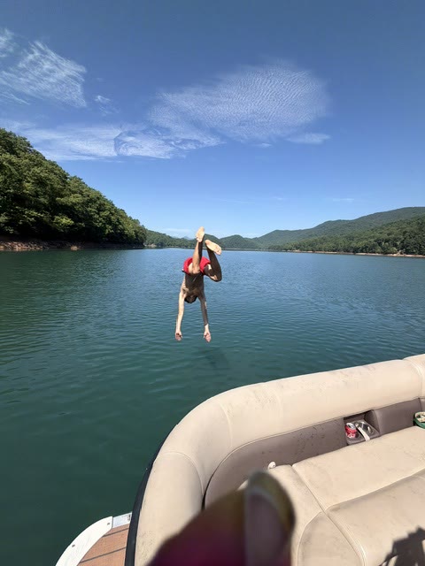 Someone diving off a boat into a blue mountain lake